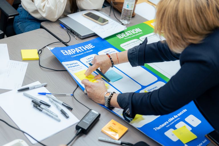 Une femme colle des post-it sur une affiche qui s'appelle 