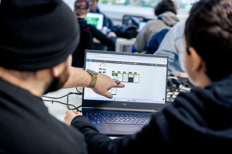 Deux jeunes hommes qui travaillent sur l'ordinateur, dont un qui montre quelque chose 